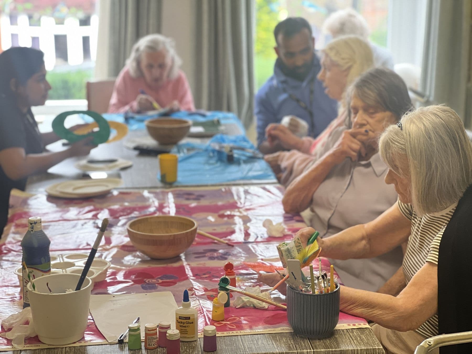 Residents painting and crafting together around a long table, with carers helping
