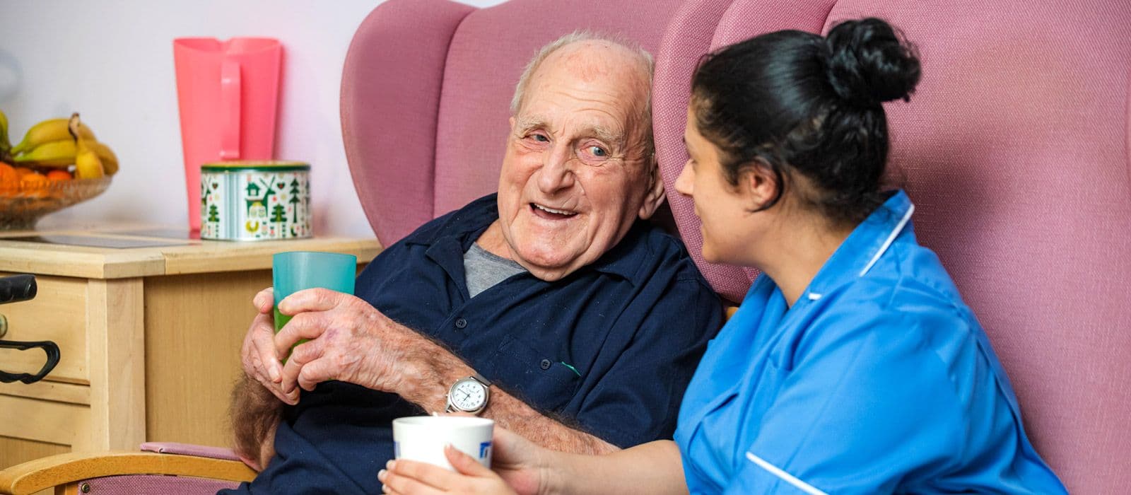 A resident sharing a laugh and a drink with a carer