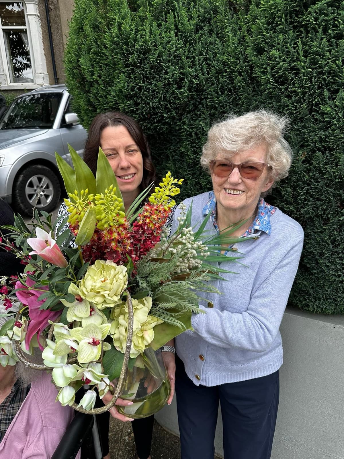 A smiling resident holding a large bouquet outside with a member of staff